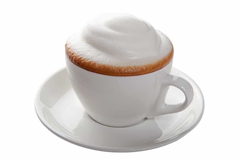 Zijaanzicht van een kop cappuccino met schuim, geserveerd op een witte schotel