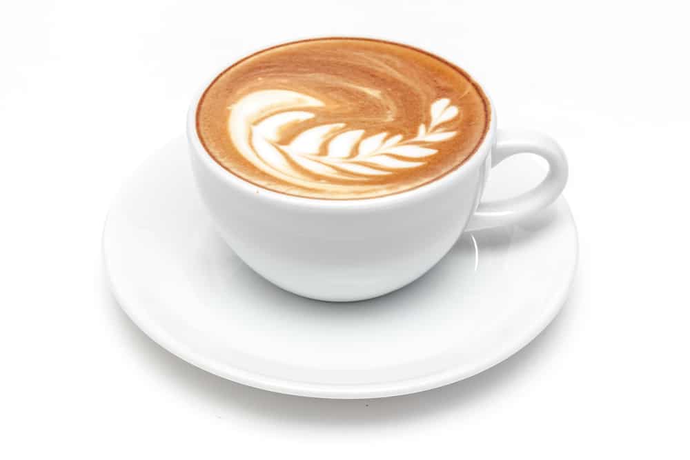 Zijaanzicht van een kop cappuccino met latte-art in de vorm van een blad, geserveerd op een witte schotel
