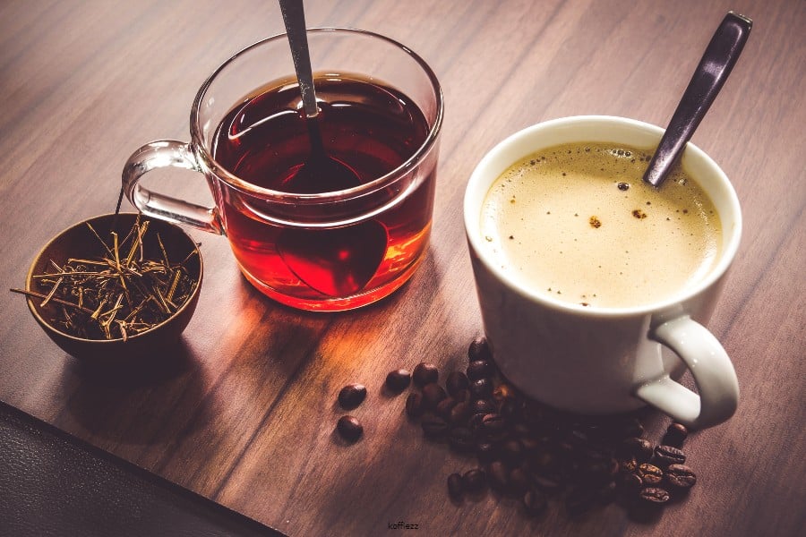 Kop koffie en glas thee op een houten tafel, met koffiebonen en losse thee ernaast