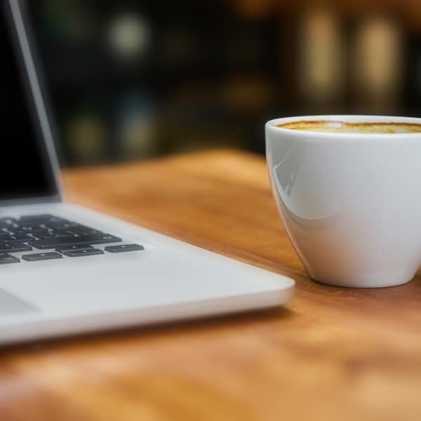 Kop koffie naast een laptop op een houten bureau